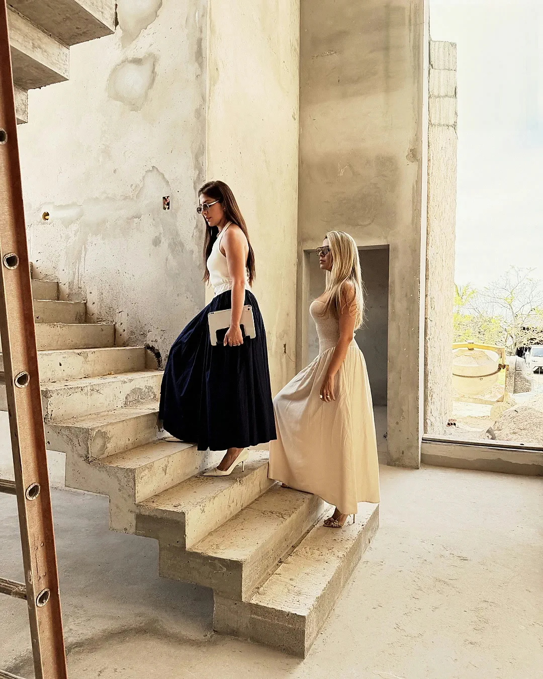 Larissa e Vanessa Amorim subindo a escada de concreto de uma obra em andamento